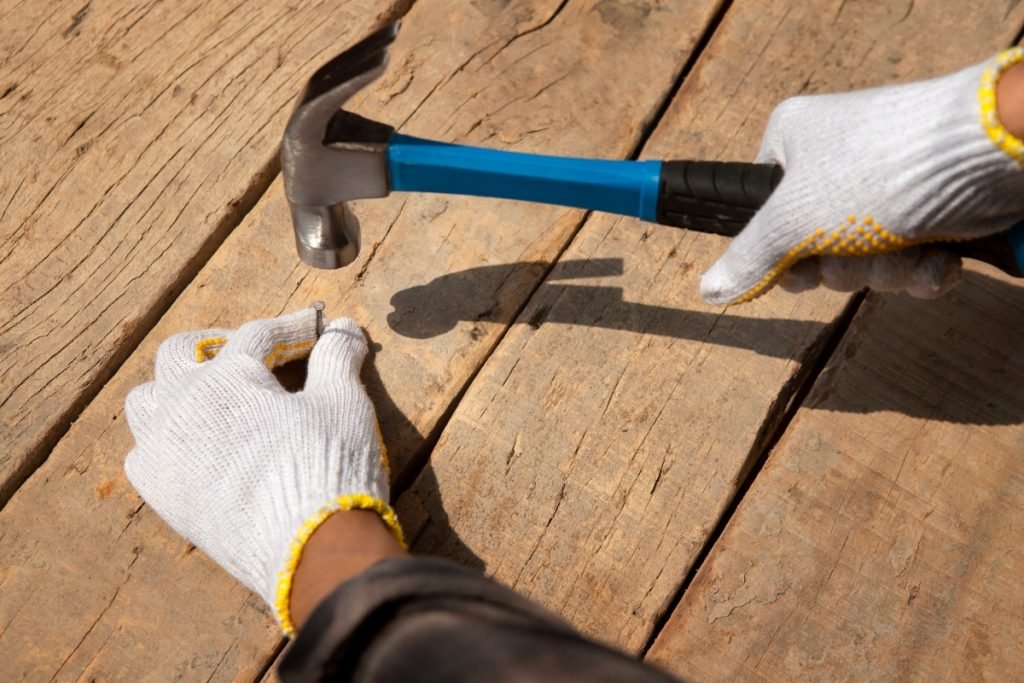 Construction worker hammering a nail into a wooden plank.