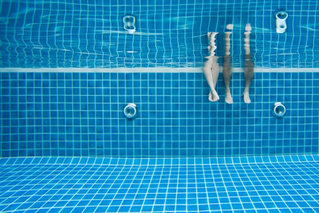 Underwater view of two people sitting at the edge of the pool with their legs in the water.