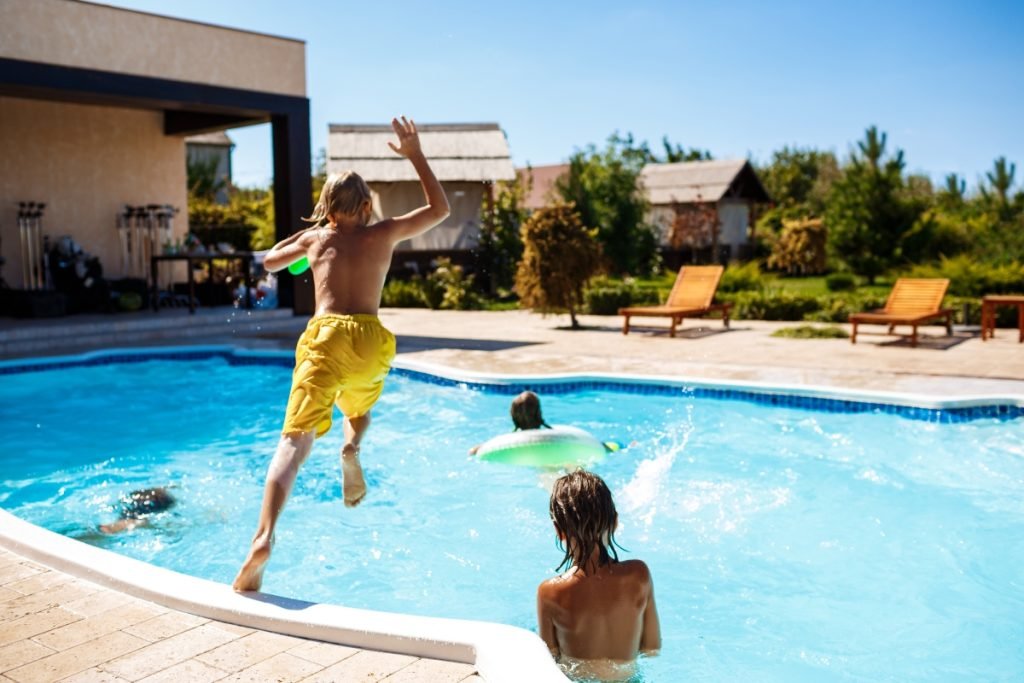 Kids jumping into a pool with a unique shape.