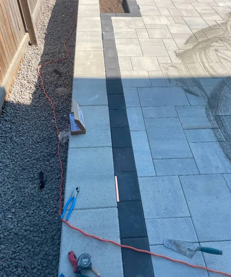 Close-up of a dark paver border band between light grey patio pavers and the outer edge course