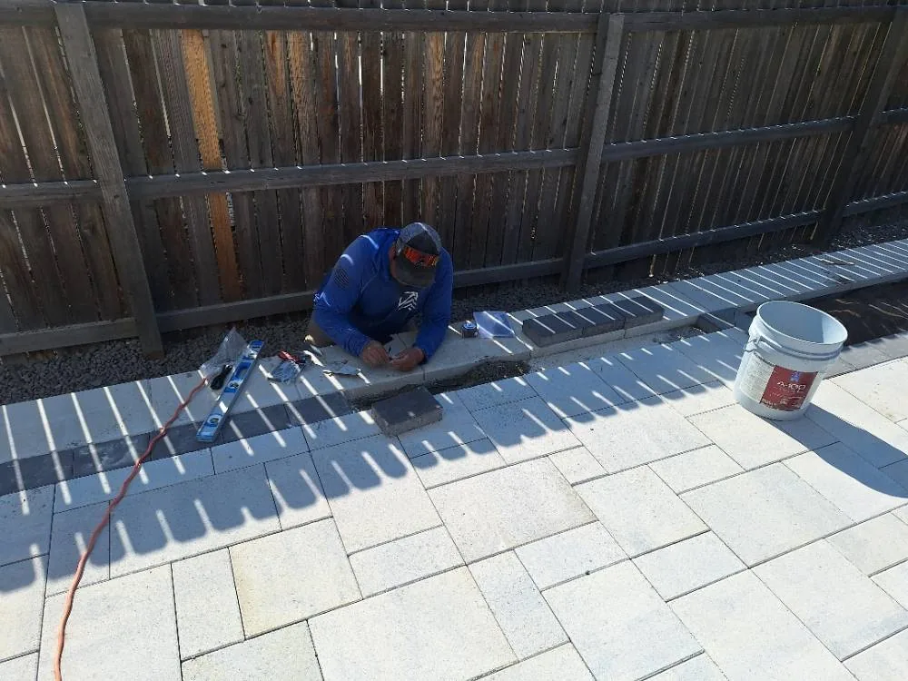 Elevate crew member setting the dark border course along the edge of a new paver patio