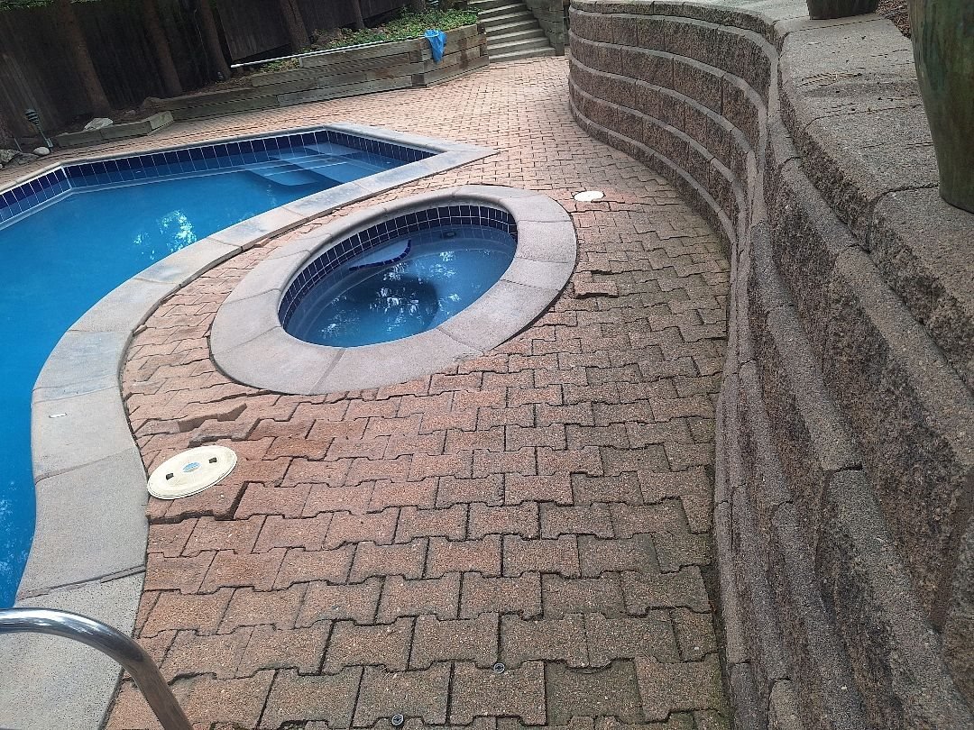 Paver pool deck around a spa next to a curved block retaining wall